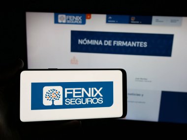 Stuttgart, Almanya - 05-04-2025: Paraguaylı sigorta şirketi Fenix Seguros 'un logosunu elinde tutan kişi web sitesinin önünde ekranda. Telefon ekranına odaklan.