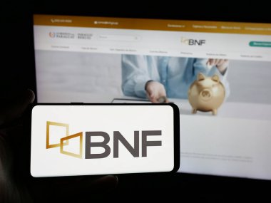 Stuttgart, Almanya - 05-04-2025: İnternet sitesi önünde Banco Nacional de Fomento (BNF) şirketinin logosuna sahip akıllı telefon sahibi kişi. Telefon ekranına odaklan.