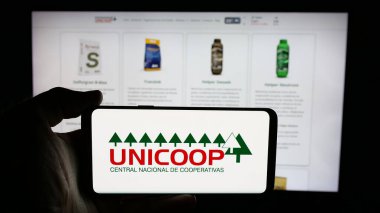 Stuttgart, Almanya - 05-04-2025: Web sayfası önünde üzerinde Union Agricola de Cooperativas (UNICOP) logosu bulunan kişi. Telefon ekranına odaklan.