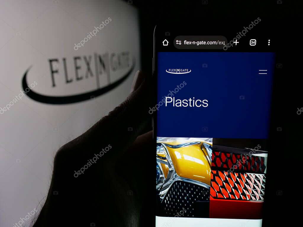 Stuttgart, Germany - 05-02-2025: Person holding cellphone with web page of US automotive company Flex-N-Gate LLC on screen in front of logo. Focus on center of phone display.