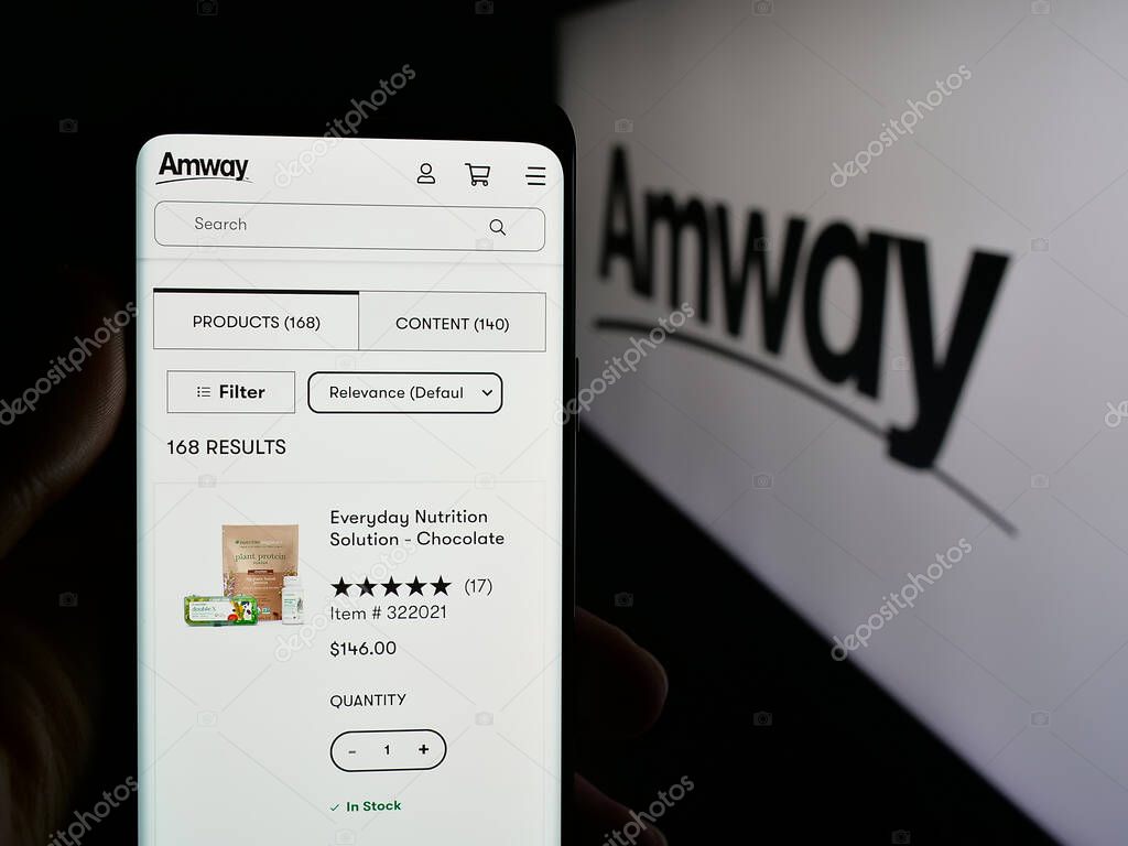 Stuttgart, Germany - 05-02-2025: Person holding cellphone with web page of US multi-level marketing company Amway Corp. on screen in front of logo. Focus on center of phone display.