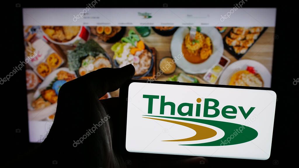 Stuttgart, Germany - 05-02-2025: Person holding mobile phone with logo of company Thai Beverage plc (ThaiBev) on screen in front of web page. Focus on phone display.