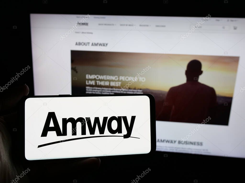 Stuttgart, Germany - 05-02-2025: Person holding smartphone with logo of US multi-level marketing company Amway Corp. on screen in front of website. Focus on phone display.