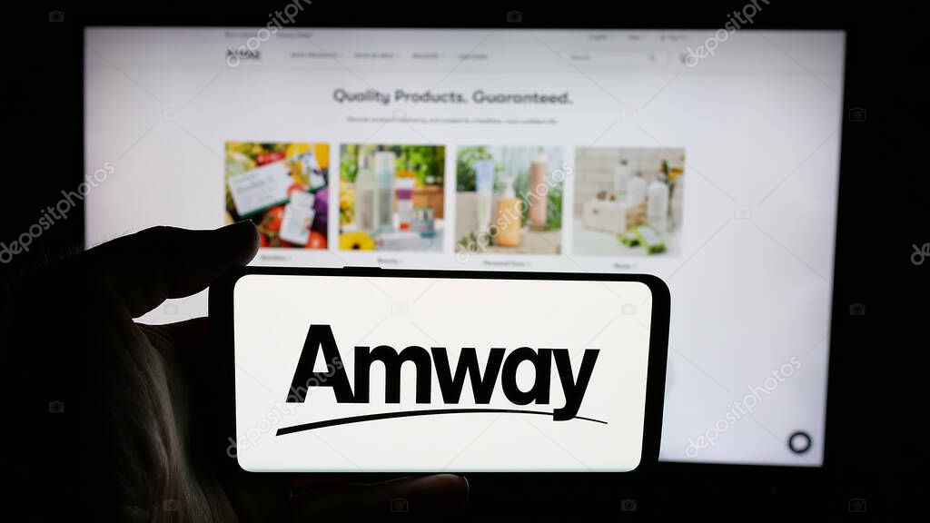 Stuttgart, Germany - 05-02-2025: Person holding cellphone with logo of US multi-level marketing company Amway Corp. on screen in front of webpage. Focus on phone display.