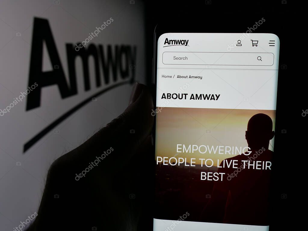 Stuttgart, Germany - 05-02-2025: Person holding smartphone with website of US multi-level marketing company Amway Corp. on screen in front of logo. Focus on center of phone display.