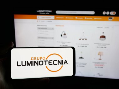 Stuttgart, Almanya - 05-04-2025: Paraguay şirketi Grupo Luminotecnia 'nın logosunu elinde tutan kişi web sitesinin önünde ekranda. Telefon ekranına odaklan.