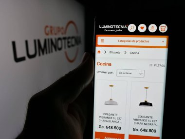 Stuttgart, Almanya - 05-04-2025: Paraguay şirketi Grupo Luminotecnia 'nın web sitesi ile akıllı telefonu olan kişi logo önünde ekranda. Telefon ekranının merkezine odaklan.