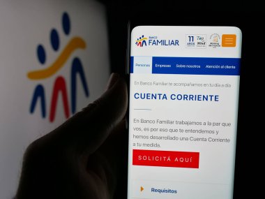 Stuttgart, Almanya - 05-04-2025: Paraguaylı finans şirketi Banco Familiar 'ın internet sitesiyle akıllı telefon sahibi kişi logo önünde ekranda görülüyor. Telefon ekranının merkezine odaklan.