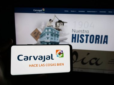 Stuttgart, Almanya - 05-05-2025: Sitenin önünde ekranda Kolombiyalı Carvajal S.A. şirketinin logosunun bulunduğu akıllı telefonu tutan kişi. Telefon ekranına odaklan.