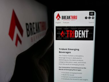Stuttgart, Almanya - 05-06-2025: Logo önünde ekranda Breakthru Beverage Group LLC logosunun logosu bulunan kişi. Telefon ekranının merkezine odaklan.