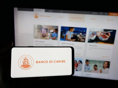 Stuttgart, Almanya - 05-06-2025: Finans hizmetleri şirketi Banco di Caribe 'nin logosunu elinde tutan kişi web sitesinin önünde ekranda. Telefon ekranına odaklan.