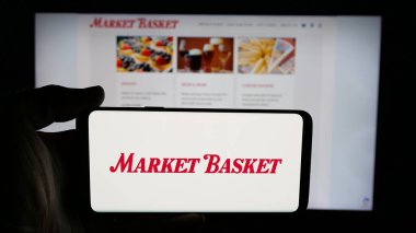 Stuttgart, Almanya - 05-07-2025: Web sayfası önünde üzerinde DeMoulas Super Markets Inc. (Pazar Sepeti) logosu bulunan cep telefonu sahibi kişi. Telefon ekranına odaklan.