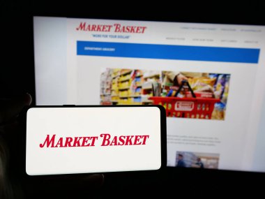 Stuttgart, Almanya - 05-07-2025: Web sitesi önünde üzerinde DeMoulas Super Markets Inc. (Pazar Basket) logosu olan akıllı telefon sahibi kişi. Telefon ekranına odaklan.
