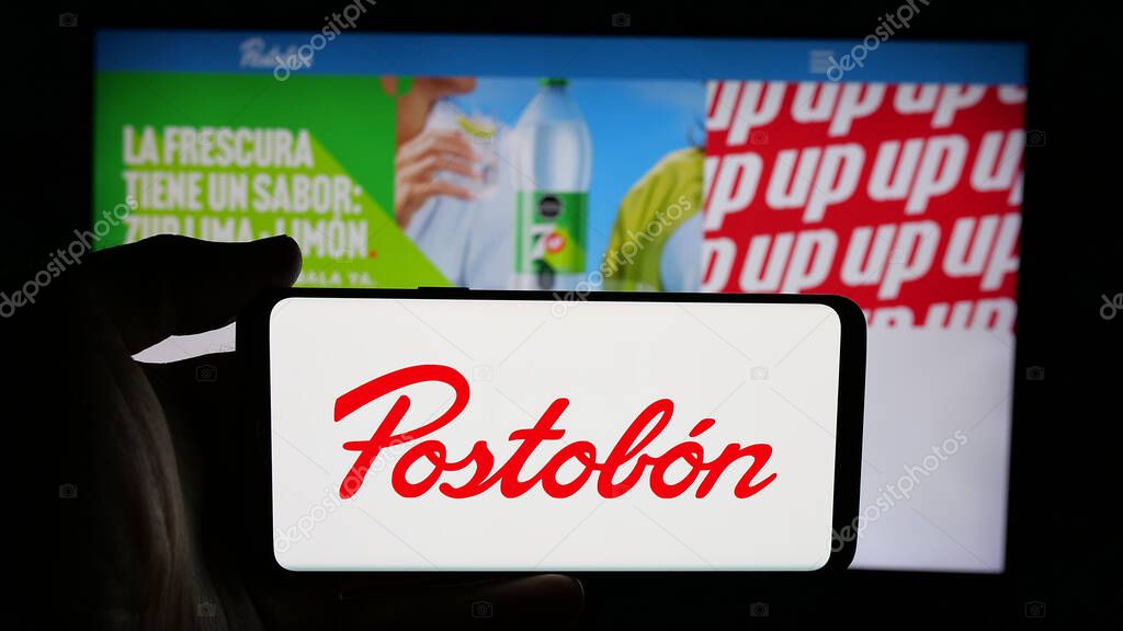 Stuttgart, Germany - 05-05-2025: Person holding cellphone with logo of Colombian beverage company Postobon S.A. on screen in front of webpage. Focus on phone display.