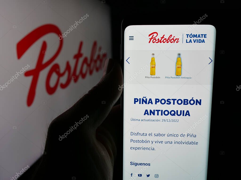 Stuttgart, Germany - 05-05-2025: Person holding web page with logo of Colombian beverage company Postobon S.A. on screen in front of logo. Focus on center of phone display.