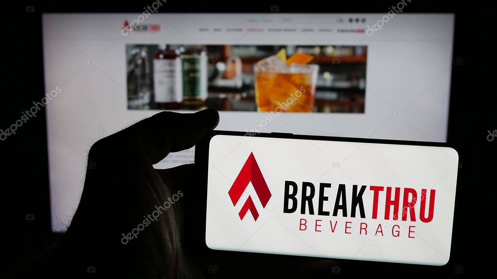 Stuttgart, Germany - 05-06-2025: Person holding mobile phone with logo of US company Breakthru Beverage Group LLC on screen in front of web page. Focus on phone display.