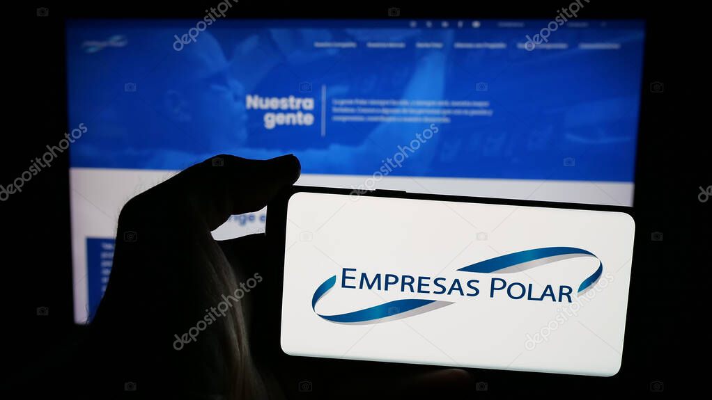 Stuttgart, Germany - 05-06-2025: Person holding mobile phone with logo of Venezuelan beverage company Empresas Polar on screen in front of web page. Focus on phone display.