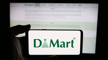 Stuttgart, Almanya - 05-14-2025: İnternet sayfası önünde üzerinde Avenue Supermart Limited (DMart) şirketinin logosu bulunan cep telefonu sahibi kişi. Telefon ekranına odaklan.