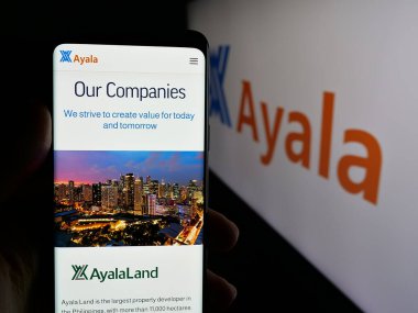 Stuttgart, Almanya - 05-14-2025: Filipinli holding şirketi Ayala Corporation 'ın web sayfası ile logo önünde cep telefonu tutan kişi. Telefon ekranının merkezine odaklan.