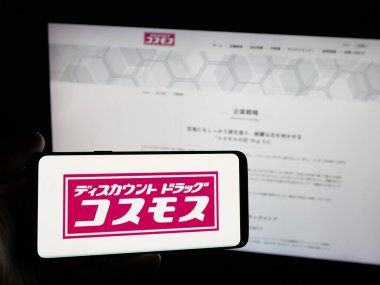 Stuttgart, Almanya - 05-14-2025: Japon firması COSMOS Pharmaceutical Corp 'un logosuna sahip akıllı telefonu web sitesinin önünde ekranda tutan kişi. Telefon ekranına odaklan.