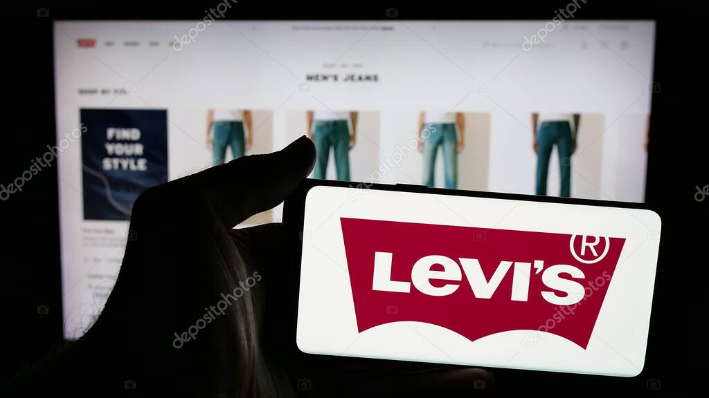 Stuttgart, Germany - 05-14-2025: Person holding mobile phone with logo of US clothing company Levi Strauss Co. (Levi's) on screen in front of web page. Focus on phone display.
