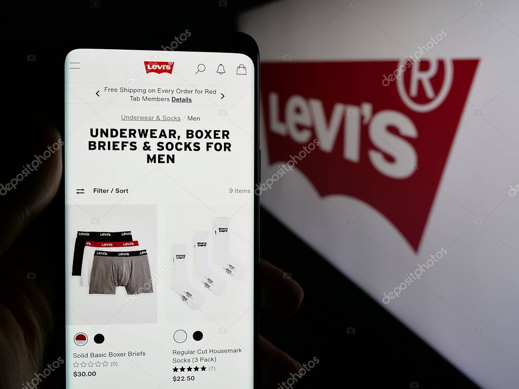 Stuttgart, Germany - 05-14-2025: Person holding cellphone with webpage of US clothing company Levi Strauss Co. (Levi's) on screen in front of logo. Focus on center of phone display.
