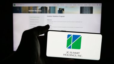 Stuttgart, Almanya - 05-14-2025: İnternet sayfası önünde JG Summit Holding Inc. (JGSHI) şirketinin logosu olan cep telefonu sahibi kişi. Telefon ekranına odaklan.