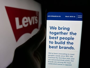 Stuttgart, Almanya - 05-14-2025: Logo önünde üzerinde ABD 'li giyim şirketi Levi Strauss Co. (Levi' s) logosu bulunan kişi. Telefon ekranının merkezine odaklan.