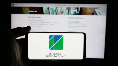 Stuttgart, Almanya - 05-14-2025: İnternet sayfası önünde JG Summit Holding Inc. (JGSHI) şirketinin logosu olan cep telefonu sahibi kişi. Telefon ekranına odaklan.