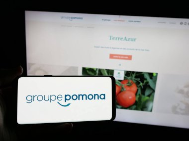 Stuttgart, Almanya - 05-15-2025: İnternet sitesinin önünde ekranda yiyecek dağıtım şirketi Groupe Pomona 'nın logosuna sahip akıllı telefon tutan kişi. Telefon ekranına odaklan.