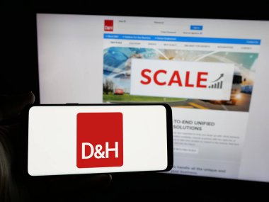 Stuttgart, Almanya - 05-15-2025: İnternet sitesi önünde üzerinde IT dağıtım şirketi DH Distributing Co. 'nun logosu bulunan akıllı telefon sahibi kişi. Telefon ekranına odaklan.