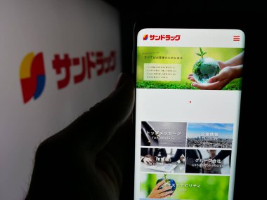 Stuttgart, Almanya - 05-16-2025: İlaç şirketi Sundrug Co. Ltd. nin web sayfası ile akıllı telefon sahibi kişi logonun önünde ekranda. Telefon ekranının merkezine odaklan.