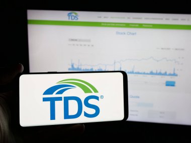 Stuttgart, Almanya - 05-16-2025: İnternet sitesi önünde üzerinde TDS (Telefon ve Veri Sistemleri Şirketi) logosu olan akıllı telefon sahibi kişi. Telefon ekranına odaklan.