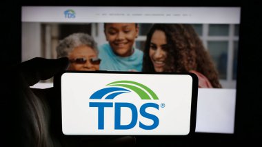 Stuttgart, Almanya - 05-16-2025: İnternet sayfası önünde üzerinde Telefon ve Veri Sistemleri Şirketi logosu bulunan cep telefonu sahibi kişi. Telefon ekranına odaklan.