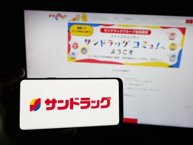 Stuttgart, Almanya - 05-16-2025: İnternet sitesi önünde üzerinde ilaç şirketi Sundrug Co. Ltd. logosu olan akıllı telefon sahibi kişi. Telefon ekranına odaklan.