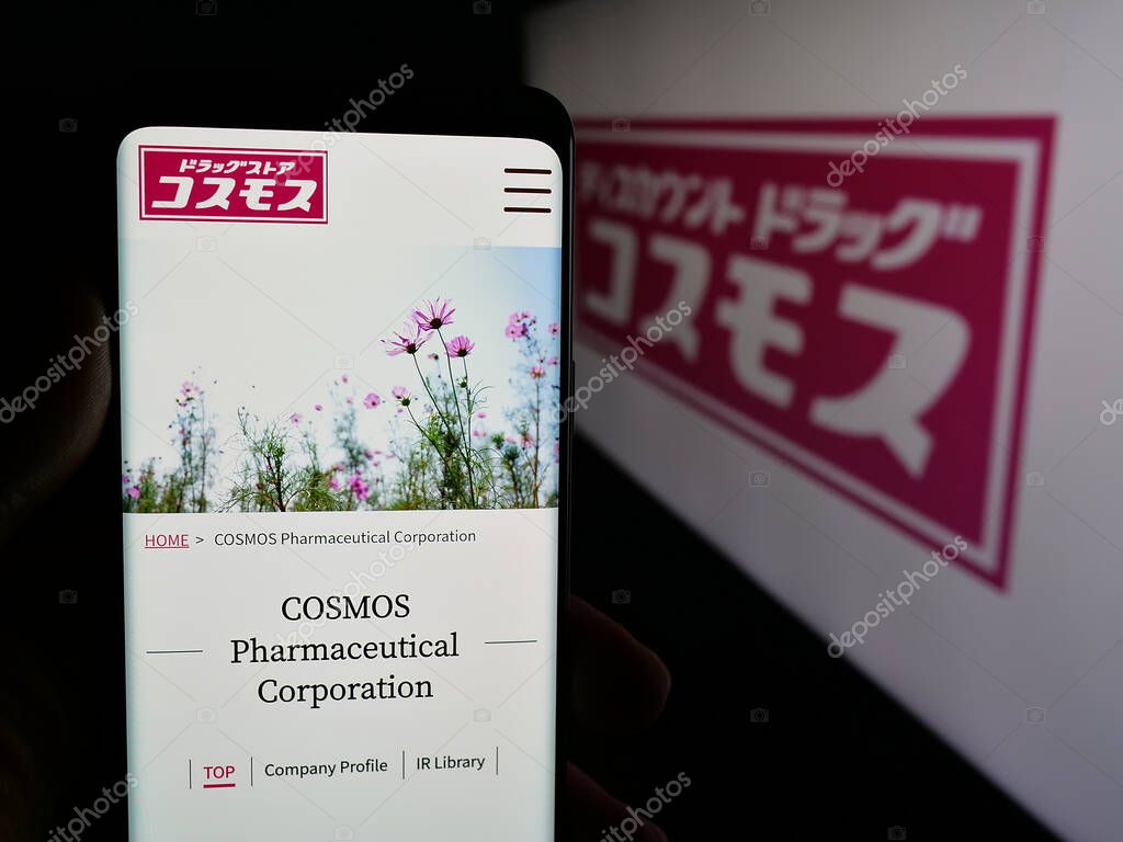 Stuttgart, Germany - 05-14-2025: Person holding cellphone with webpage of Japanese company COSMOS Pharmaceutical Corp. on screen in front of logo. Focus on center of phone display.