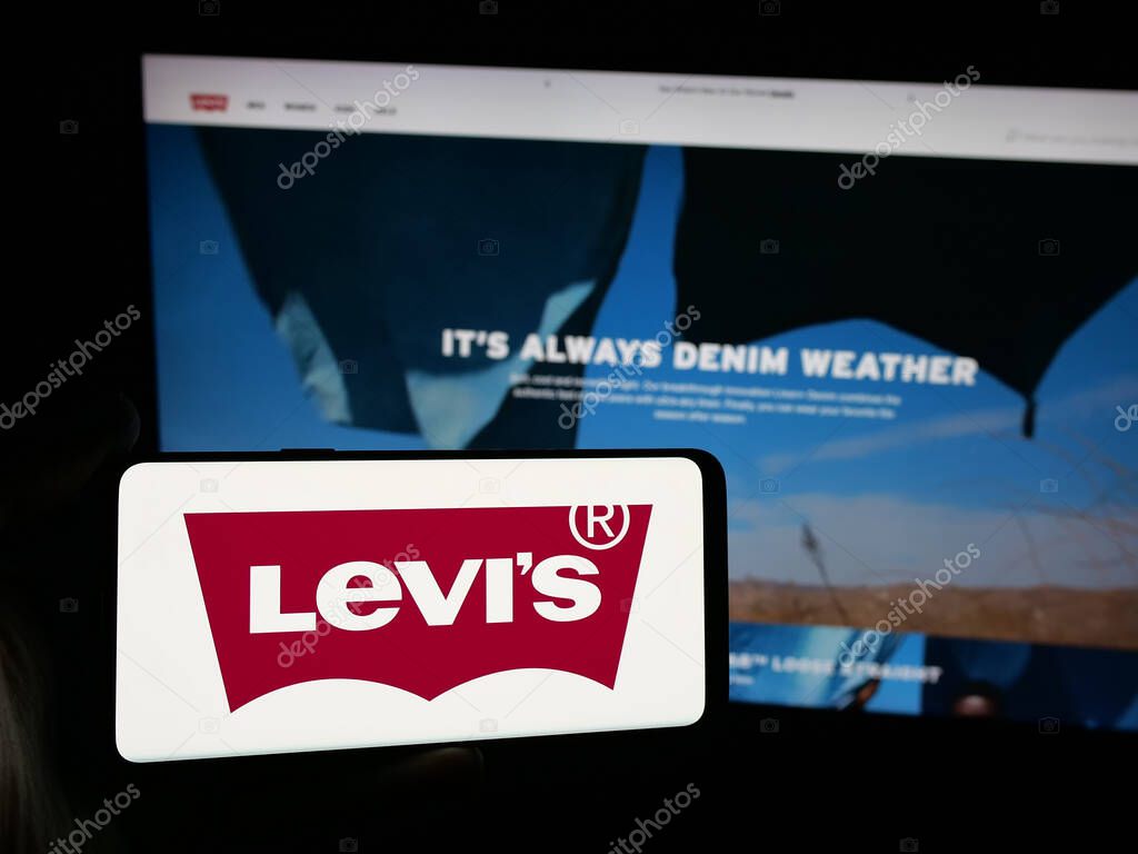 Stuttgart, Germany - 05-14-2025: Person holding smartphone with logo of US clothing company Levi Strauss Co. (Levi's) on screen in front of website. Focus on phone display.