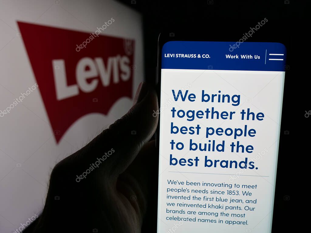 Stuttgart, Germany - 05-14-2025: Person holding web page with logo of US clothing company Levi Strauss Co. (Levi's) on screen in front of logo. Focus on center of phone display.