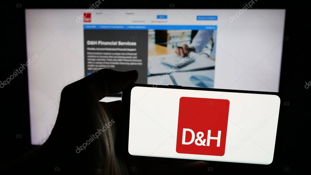 Stuttgart, Germany - 05-15-2025: Person holding mobile phone with logo of IT distribution company DH Distributing Co. on screen in front of web page. Focus on phone display.