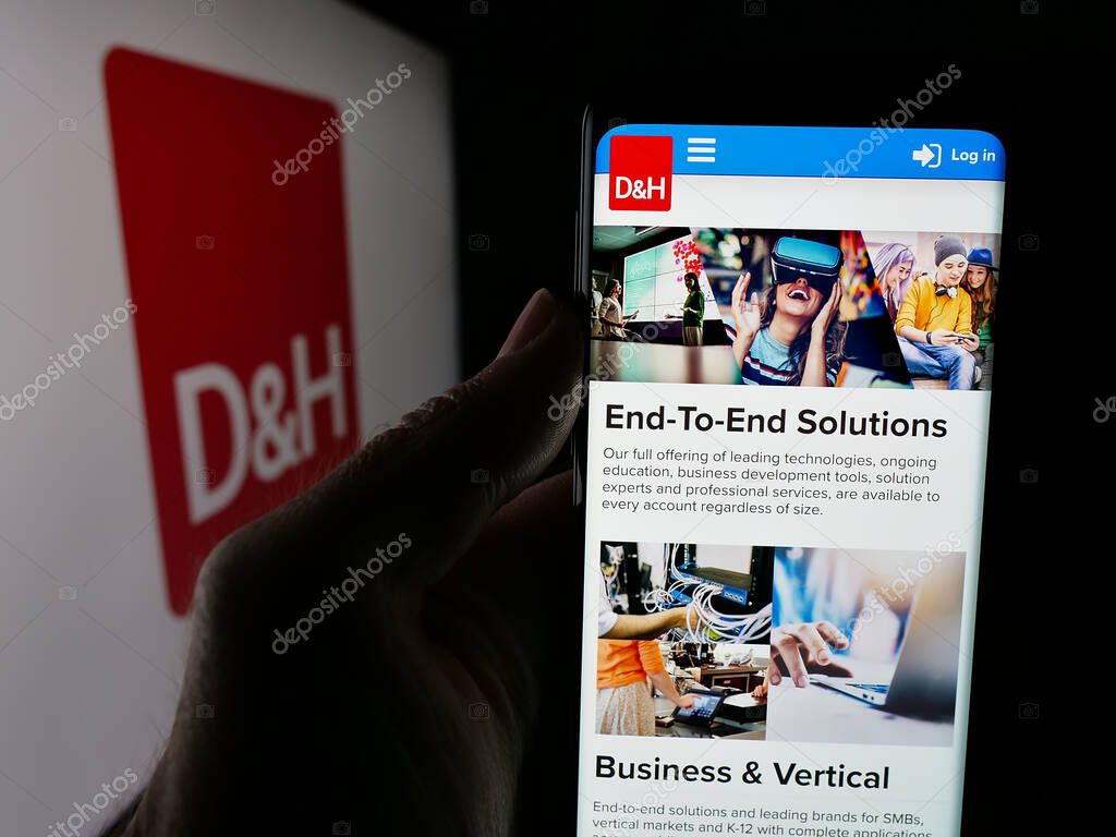 Stuttgart, Germany - 05-15-2025: Person holding smartphone with web page of IT distribution company DH Distributing Co. on screen in front of logo. Focus on center of phone display.