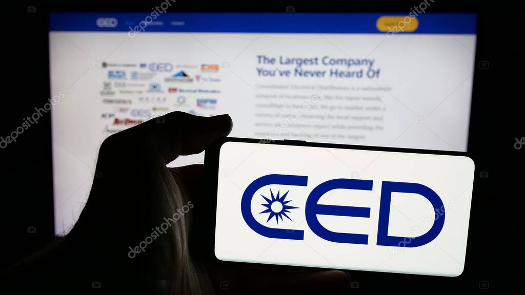 Stuttgart, Germany - 05-15-2025: Person holding mobile phone with logo of Consolidated Electrical Distributors (CED) on screen in front of web page. Focus on phone display.