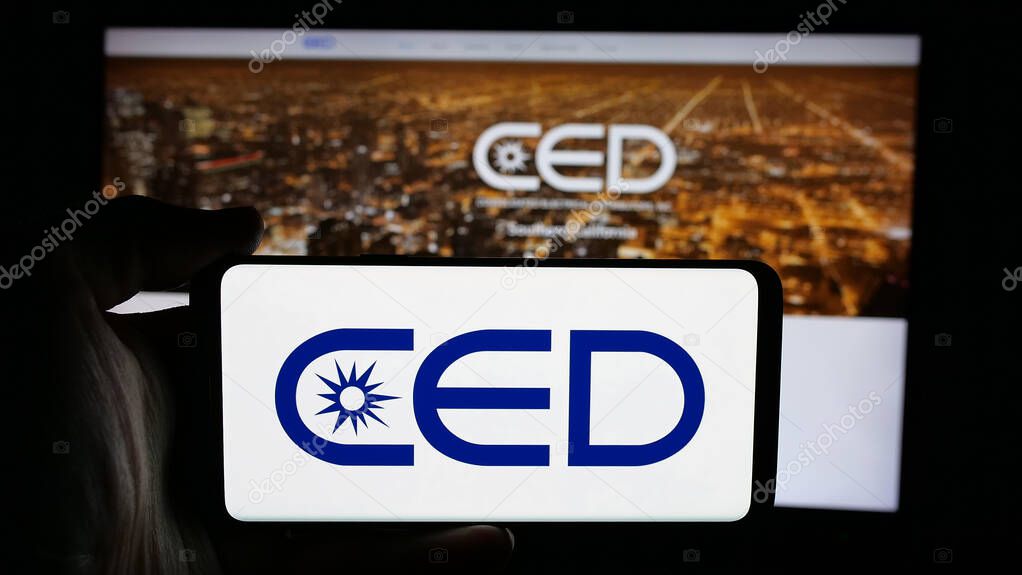 Stuttgart, Germany - 05-15-2025: Person holding cellphone with logo of Consolidated Electrical Distributors (CED) on screen in front of webpage. Focus on phone display.