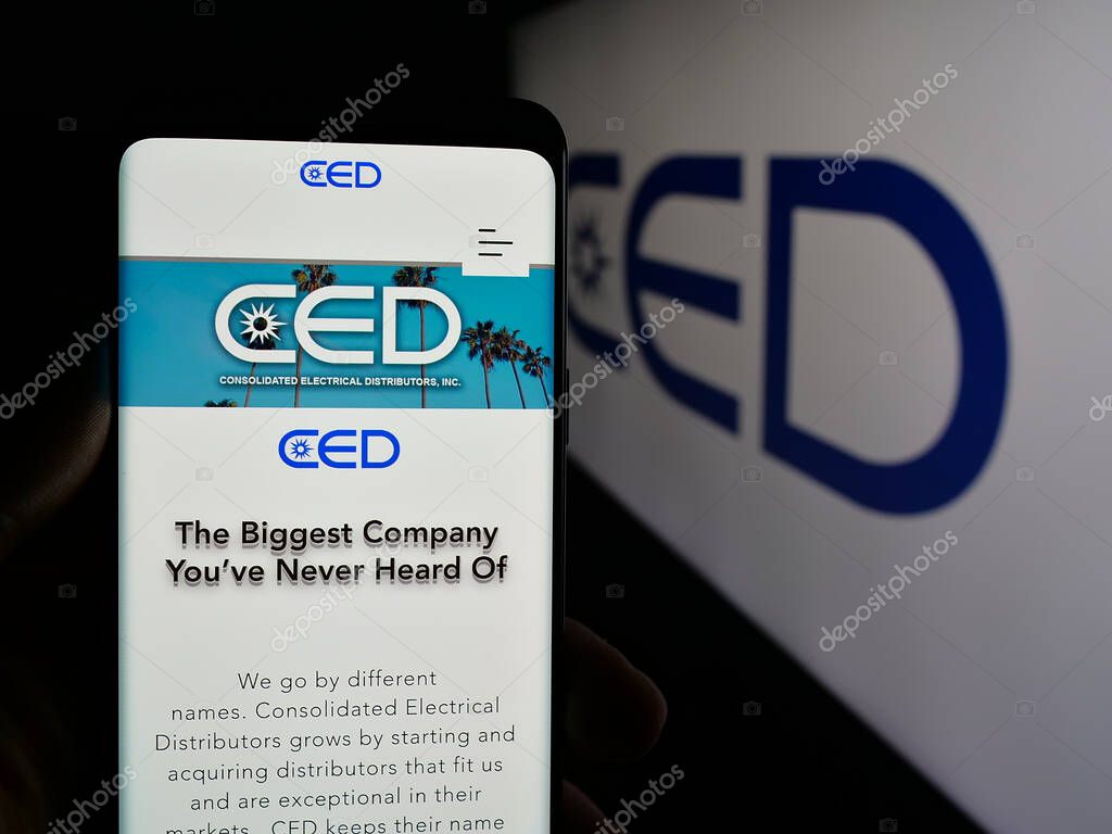 Stuttgart, Germany - 05-15-2025: Person holding smartphone with web page of Consolidated Electrical Distributors (CED) on screen in front of logo. Focus on center of phone display.