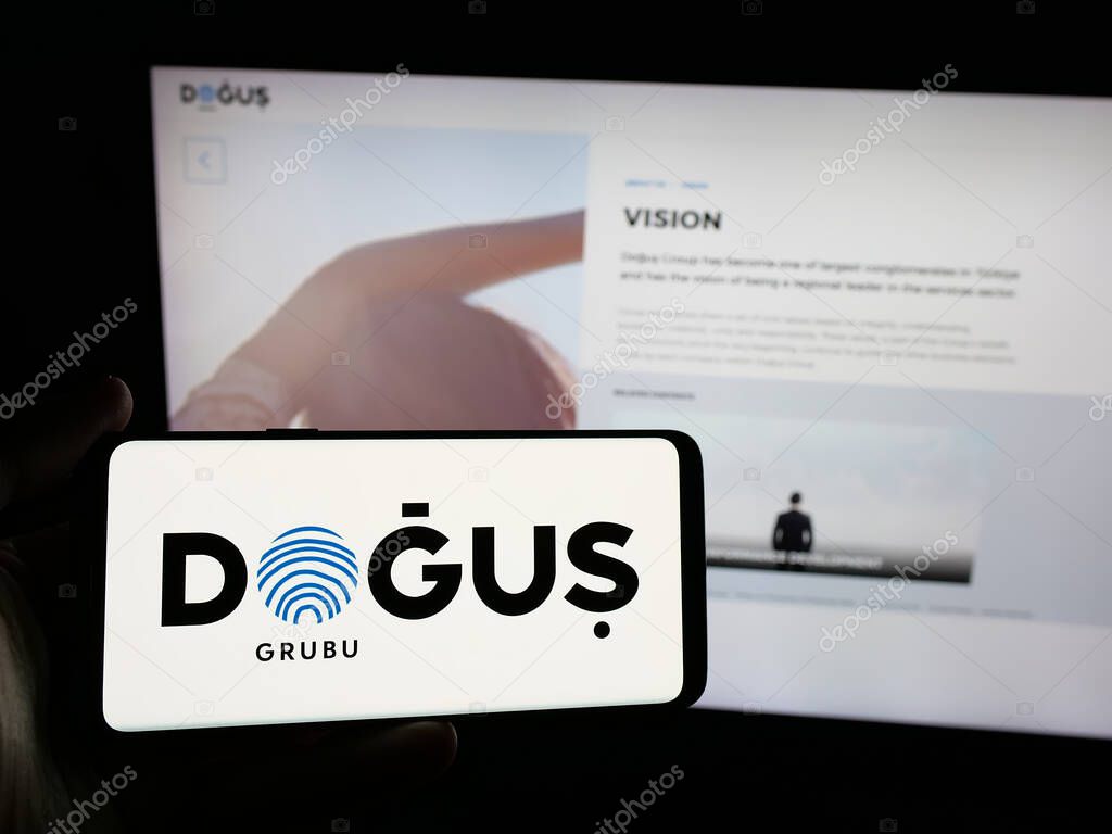 Stuttgart, Germany - 05-16-2025: Person holding smartphone with logo of Turkish company Dogus Holding A.S. on screen in front of website. Focus on phone display.