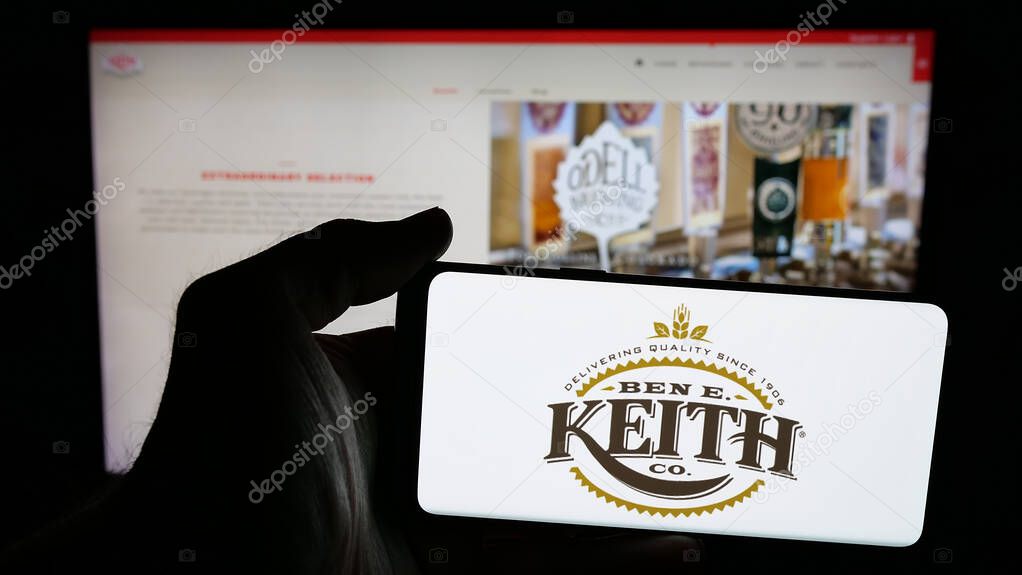 Stuttgart, Germany - 05-16-2025: Person holding mobile phone with logo of US distribution business Ben E. Keith Company on screen in front of web page. Focus on phone display.