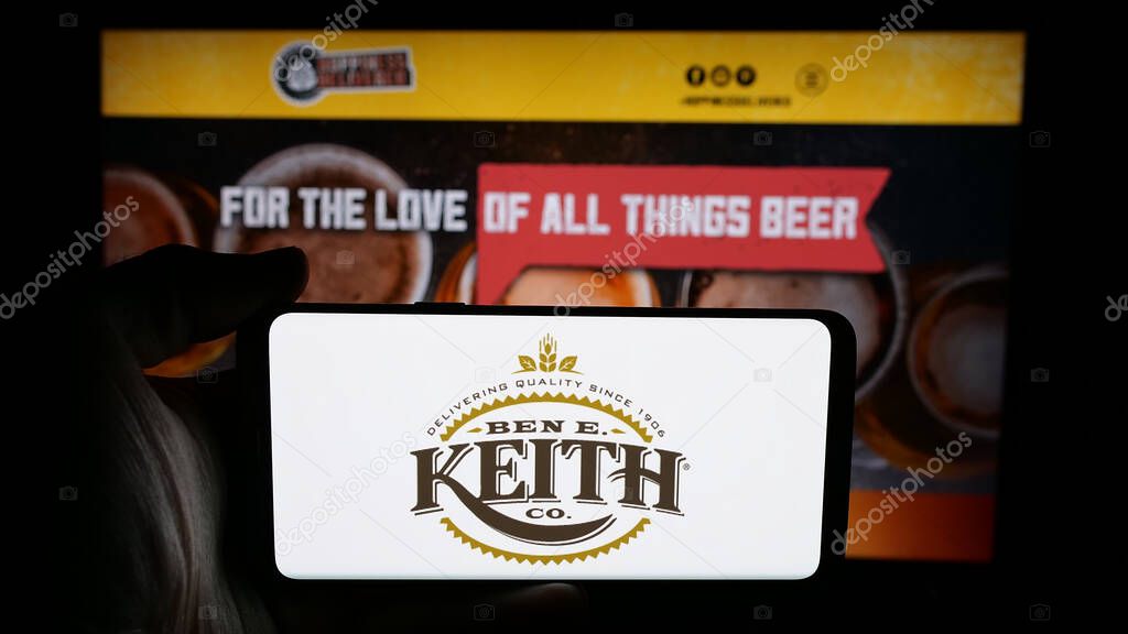Stuttgart, Germany - 05-16-2025: Person holding cellphone with logo of US distribution business Ben E. Keith Company on screen in front of webpage. Focus on phone display.