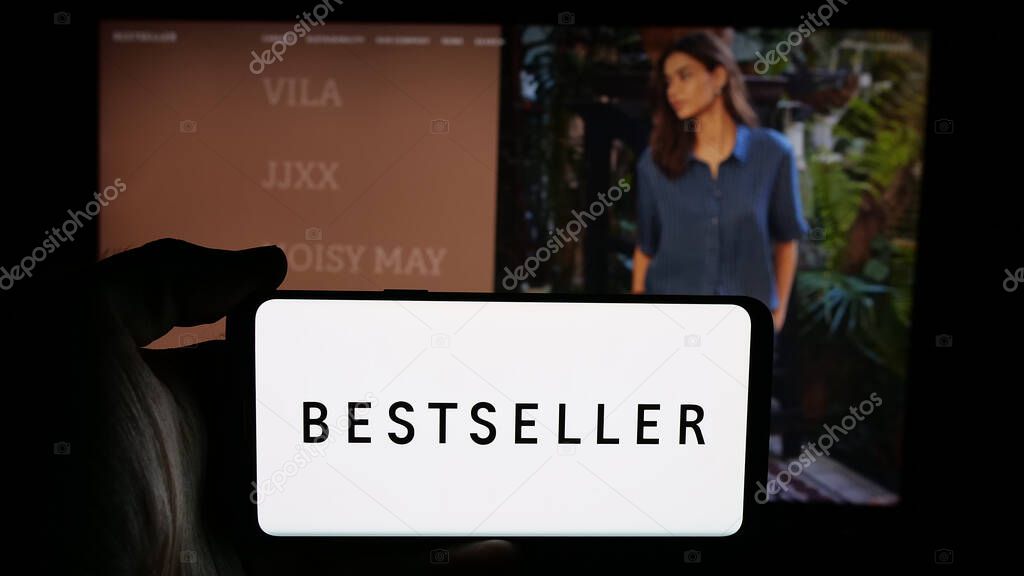 Stuttgart, Germany - 05-16-2025: Person holding cellphone with logo of Danish clothing company Bestseller AS on screen in front of webpage. Focus on phone display.
