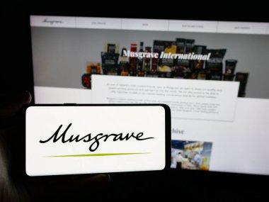 Stuttgart, Almanya - 05-17-2025: İrlandalı gıda şirketi Musgrave Group Ltd. 'nin logosunu elinde tutan kişi web sitesinin önünde ekranda. Telefon ekranına odaklan.