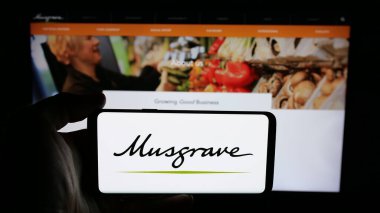 Stuttgart, Almanya - 05-17-2025: İrlandalı gıda şirketi Musgrave Group Ltd. 'nin logosunu elinde tutan kişi web sayfasının önünde ekranda. Telefon ekranına odaklan.