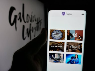Stuttgart, Almanya - 05-17-2025: Alışveriş merkezi şirketi Galeries Lafayette 'in web sayfası ile birlikte logo önünde cep telefonu tutan kişi. Telefon ekranının merkezine odaklan.